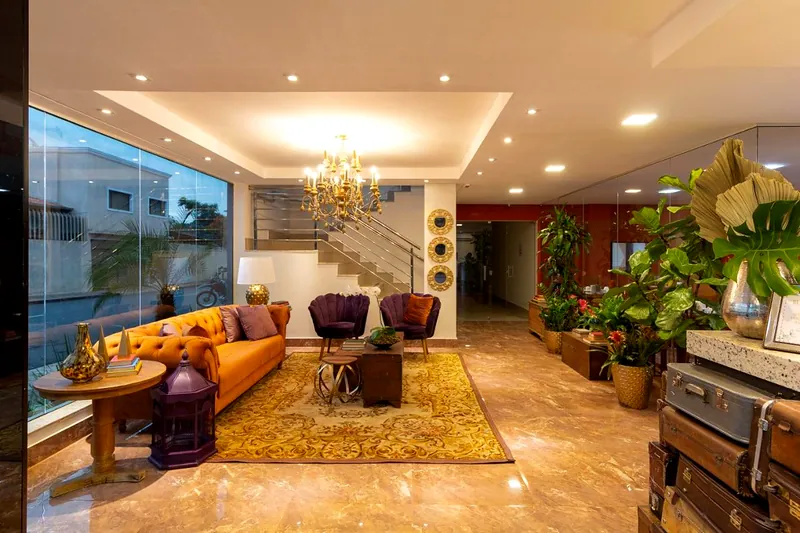 Lobby com sofá laranja, poltronas cor de ameixa, lustre dourado e escada