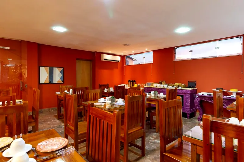Salão do café da manhã com mesas de madeira e paredes terracota