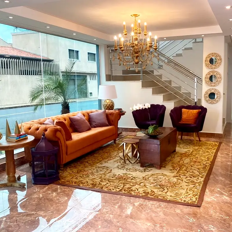 Sala de estar do lobby com lustre dourado, escada de vidro e sofá chesterfield laranja